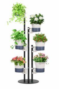 Vertical indoor plant stand with six potted plants, featuring trailing greenery and flowering plants arranged on a freestanding metal pole system.